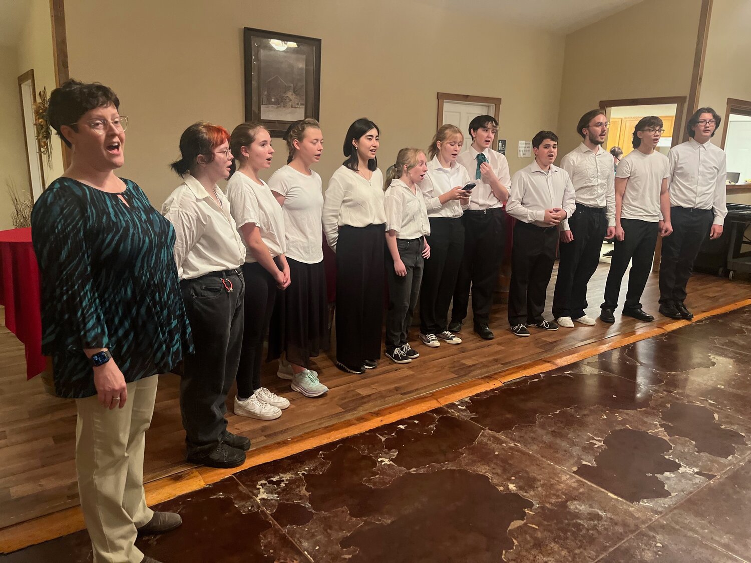 The Mid-Prairie high school choir, directed by vocal director Collette McClellen, left, sang at the end of the Chef Spotlight Fundraiser Dinner.  Students shown here: Toby Olson, Georgia White, Phoebe Shetler, Faziia Kasymova, Jillian Clark, Wren Harris, Isadora Goode, Logan McClellen, Jimmy Rempel, Lincoln Wulf, and Brock Lowenberg.  Not pictured: Kali Miller.